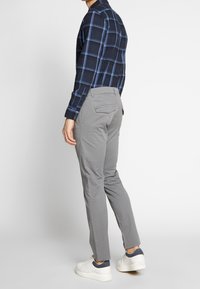 Marineblaues Karoshirt mit blauen Akzenten, kombiniert mit hellgrauen, schmal zulaufenden Hosen und weißen Sneakers. Der Stoff wirkt weich mit einer glatten Textur.