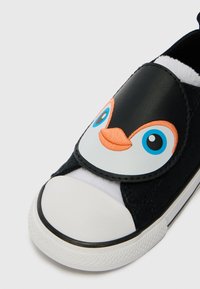 Mustat liukupohjaiset kengät, jotka on valmistettu kankaasta ja synteettisistä materiaaleista. Kengissä on pingviinin kasvokuvio, jossa on siniset silmät ja oranssi nokka; valkoinen varvasosa.