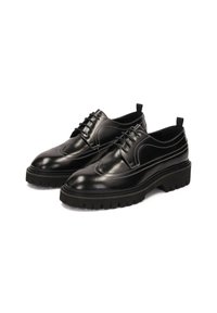 Zapatos de cuero negro con acabado pulido; diseño tipo "wingtip", costuras blancas y una suela de goma texturada gruesa para mayor agarre.