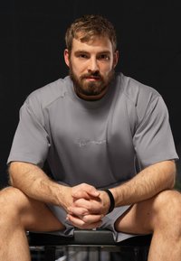 T-shirt de sport gris à manches courtes avec un col rond et un logo brodé, assorti à un short. Tissu uni et coupe décontractée.