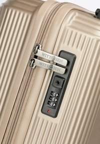Beige harde koffer met reliëf-ribbels, dubbele ritssluitingen met het label "WITTCHEN" en een zwarte TSA-combinatieslot.