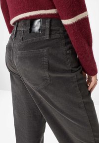 Grauige Cordhose mit vertikalen Rippungen, ausgestattet mit Gesäßtaschen und einem schwarzen Leder-Label am Bund.