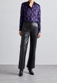 Lila blumenmusterte Satin-Bluse mit Kragen, langen Ärmeln, kombiniert mit hoch taillierten schwarzen Leder-Hosen mit Schlag und spitzen schwarzen Stiefeln.