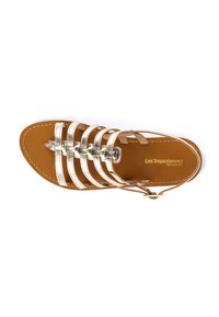 Flat sandals featuring metallic gold straps with an open design. Brown leather footbed. Buckle accent on ankle strap.