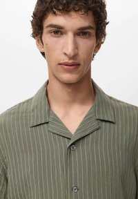 Short-sleeve olive green shirt with vertical stripes, notched collar, and two buttons at the front. Lightweight fabric, relaxed fit.