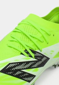 Crampons de football vert fluo avec un revêtement texturé, des rayures noires et des lacets plats, conçus pour une traction sur le terrain.
