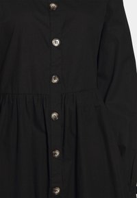 Černé šaty košilového stylu s uzavíráním na knoflíky, nařaseným pasem a dlouhými rukávy. Vyrobeno z hladkého materiálu s jemnou texturou.