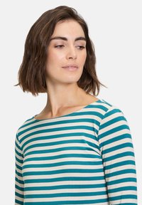 Randig långärmad tröja med turkosa och krämfärgade horisontella ränder, rund halsringning och mjukt tyg med en figurnära design.