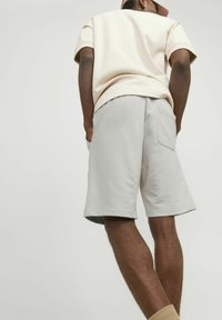 Camisa de manga corta color beige claro combinada con pantalones cortos grises claros que tienen un bolsillo trasero, textura suave y un ajuste relajado.