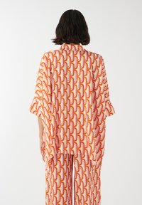 Top estilo kimono con un patrón colorido y mangas fluidas, que presenta un diseño retro de cadenas en tonos rosa, naranja y amarillo sobre un fondo claro.