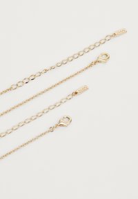Tre catene d'oro di lunghezze diverse con chiusure a morsi, caratterizzate da una superficie liscia e un design a maglie intrecciate, che mostrano una finitura lucida.