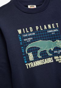 Granatowy sweatshirt z grafiką T. rexa, z niebieskimi detalami w kratkę i białym napisem, wykonany z bawełny, zaprojektowany dla dzieci.