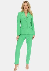 Zielony, dopasowany garnitur z dobrze skrojoną marynarką, klapami w kształcie notcha i dwoma guzikami. Spodnie w fasonie slim fit o gładkiej fakturze i bez widocznych wzorów.