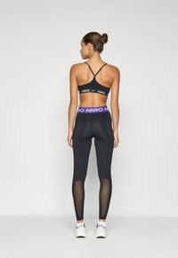 Černý sportovní podprsenka s nastavitelnými ramínky, se znakem Nike. Černé legíny s průhlednými bočními panely a kontrastním fialovým pasem.