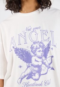 Balta medvilninė marškinėlių kolekcija su violetine grafika, vaizduojančia cherubą su sparnais, laikantį lanką ir strėlę, su tekstu "Nesuteikiu savo ANGELO Širdies lūžių klubui."