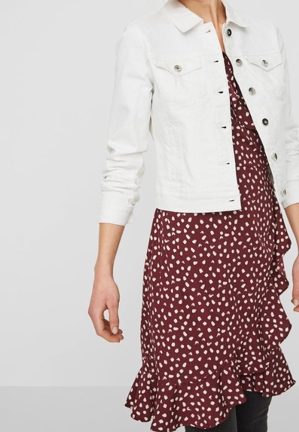 Bílá džínsová bunda s límečkem a knoflíkovým zapínáním, nošená přes burgundské šaty s bílým puntíkovým vzorem a volánkovým lemem.