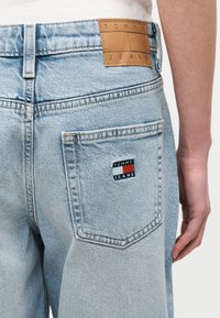 Φωτεινά μπλε τζιν από denim με πίσω τσέπη που εμφανίζει το λογότυπο Tommy Jeans και καφέ δερμάτινη ετικέτα Tommy Jeans στη μέση.