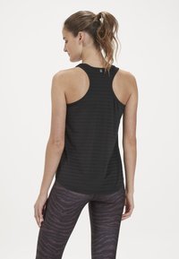Svart atletisk linne med ribbad struktur och racerback-design, ihopparat med mönstrade lila leggings med tigerrandigt mönster.