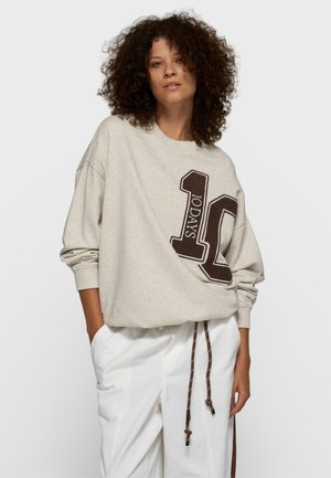 Jasnobeżowa bluza z dużym brązowym napisem "10DAYS". Luźny krój, opuszczone ramiona, ściągacze przy rękawach oraz regulowany sznurek u dołu.