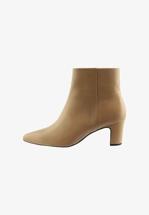 Bottine en cuir beige avec un bout pointu, une texture lisse et un talon bloc de hauteur intermédiaire ; sans quincaillerie ni embellissements visibles.