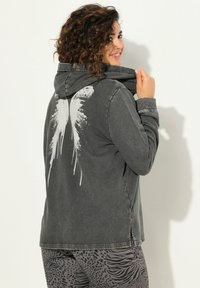Sudadera con capucha de tela gris oscuro con un diseño de salpicaduras blancas en la parte posterior. Tejido suave con un ajuste relajado y aberturas laterales.