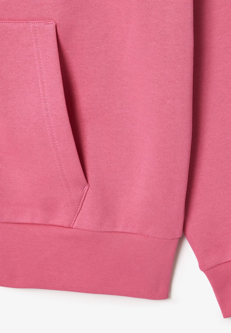 Tessuto di felpa rosa con tasca a marsupio, polsini e bordi a costine. Texture liscia con cuciture uniformi e un colore coerente in tutto il capo.