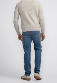 Pull en tricot beige à texture tachetée, jean en denim gris, et baskets gris clair avec une semelle en caoutchouc marron. Vue arrière de la tenue.