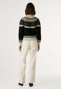 Pull en maille avec un motif zigzag noir et gris, doté d'un col et de poignets côtelés, associé à un jean droit écru.