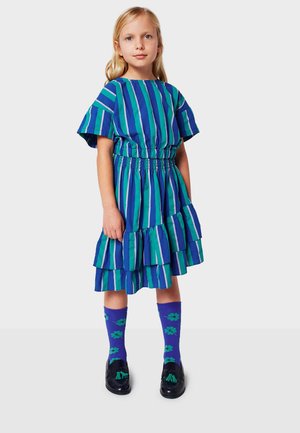 Striped dress with short sleeves in green and blue, gathered waist, and tiered skirt. Paired with purple socks featuring flower patterns.