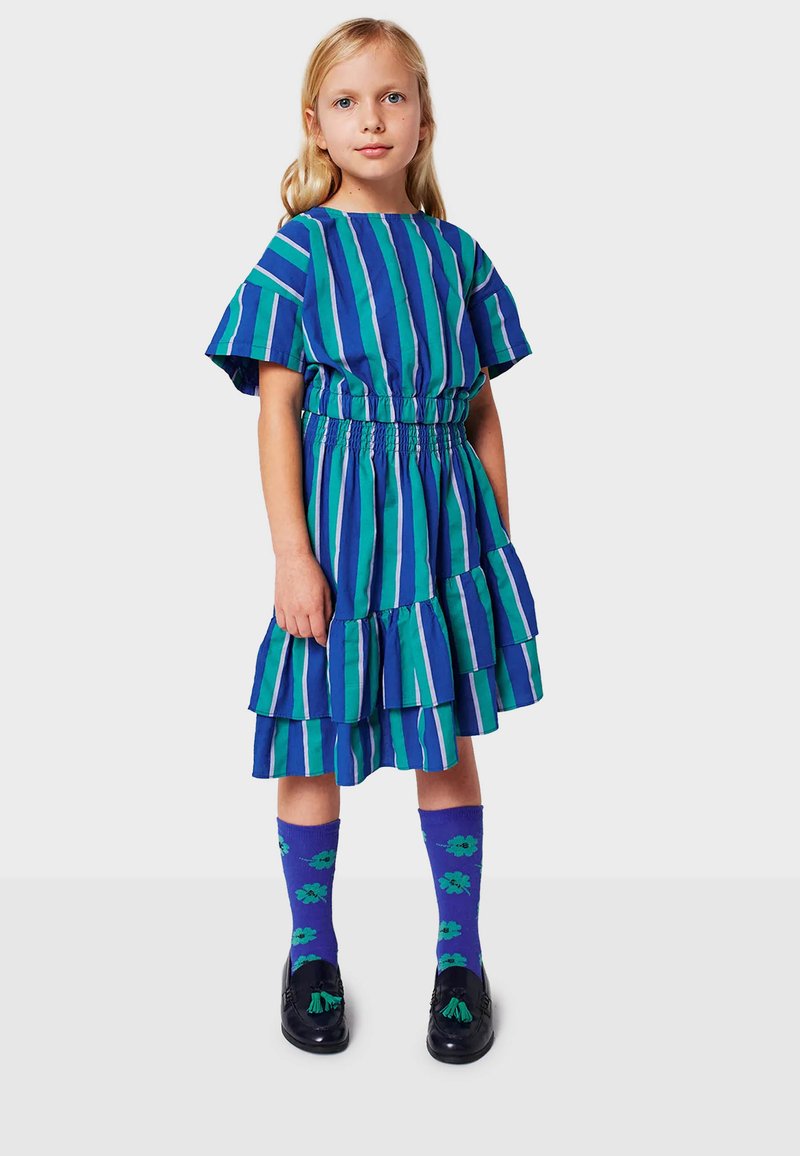 Abito a righe con maniche corte in verde e blu, vita arricciata e gonna a strati. Abbinato a calzini viola con motivi floreali.