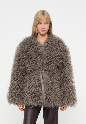 Purvinas, rudas, per didelis paltas su tekstūriška, pūkuota paviršiumi ir plačiomis rankovėmis, juosmenyje susiaurintas plonu pilku diržu.