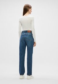 Jeans din denim albastru, cu talie înaltă și croială lejeră, design cu cinci buzunare și o etichetă din piele maro în spate, asortați cu adidași albi.