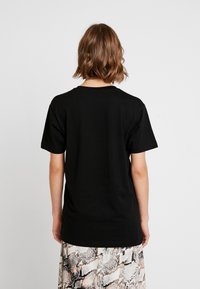 Czarna bawełniana koszulka z krótkim rękawem i okrągłym dekoltem, widok od tyłu. Nosi się ją na wzorzystą, lekką, zwiewną spódnicę.