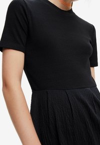 Schwarzes geripptes T-Shirt mit kurzen Ärmeln und Rundhalsausschnitt, kombiniert mit einem ausgestellten Rock aus strukturiertem schwarzem Stoff, der dezente Falten aufweist.