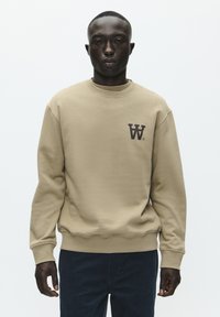 Beige sweatshirt med rund hals og ribbede manchetter. Har et mørkebrunt logo på venstre bryst. Glat tekstur, afslappet pasform.