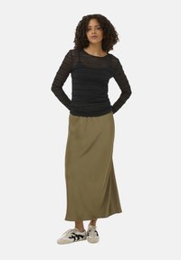 Un haut à manches longues noir à rayures associé à une jupe olive longueur genoux et des baskets blanches avec accents noirs, sur fond uni.