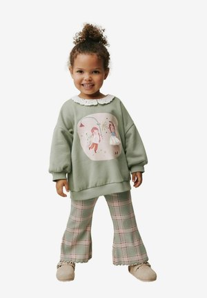 Green sweatshirt with a white lace collar, featuring an illustration. Paired with plaid flared pants in green and red tones. Beige slippers.