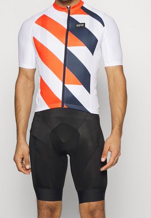 Man draagt een fietsshirt met korte mouwen met diagonale rode, witte en zwarte strepen en zwarte gevoerde fietsshorts.