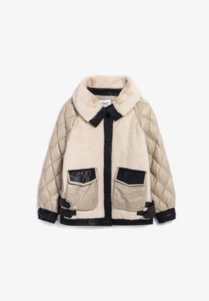 Chaqueta en beige y negro que presenta un material suave, parecido a la piel de un pelaje, en el cuerpo, mangas acolchadas con un diseño acolchado y grandes bolsillos de cuero sintético negro.