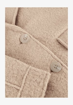 Beige textured fabric with a soft, fuzzy appearance. Features two round, light-colored buttons and stitched details on the edges.