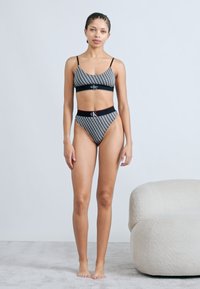 Μπικίνι σετ με ασπρόμαυρο μοτίβο και ρυθμιζόμενους ιμάντες, με ψηλόμεσο κάτω μέρος και λογότυπα στη ζώνη και το πάνω μέρος.