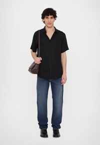 Μαύρο κοντομάνικο πουκάμισο με κουμπιά, μπλε τζιν και μαύρα παπούτσια. Το άτομο κρατά μια καφέ δερμάτινη τσάντα ώμου. Απλός σχεδι�ασμός, άνετη εφαρμογή.