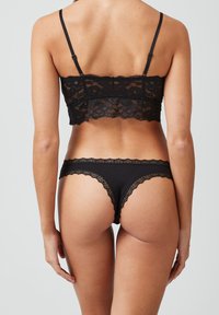 Zwart kanten bralette en bijpassende string; heeft gegolfde randen, delicate bloemmotieven en verstelbare bandjes voor een goede pasvorm.