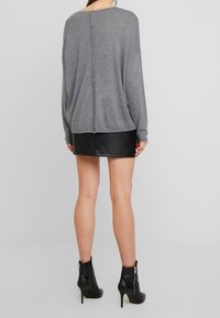 Harmaa rento neule, jossa on nappikiinnitys selässä, yhdistetty mustaan tekonahkahameeseen ja nilkkureihin. Pehmeä rakenne, arkinen tyyli.