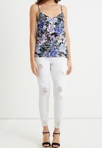 Blommig linne med svart bakgrund och lila blommor, kombinerat med slitna vita skinny jeans och svarta sandaler med remmar.