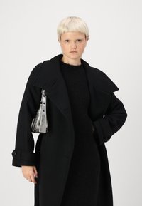 Casaco de lã preto com colarinho largo, apresentando botões grandes e um corte descontraído. Acompanhado por uma bolsa metálica prateada com uma alça para o ombro.