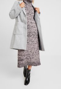 Gray wool blend coat with large pocket, worn over a knitted dress in a pink and gray pattern. Black ankle boots complete the outfit.