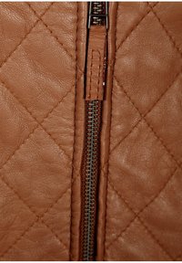 Primo piano di un cuoio marrone trapuntato con una cerniera, dotata di un tirante metallico e una cucitura a contrasto lungo la cucitura. Texture liscia.