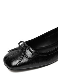 Melnas baleta kurpes, izgatavotas no spīdīga ādas materiāla. Tām ir apaļa purngala forma, ar loku akcentu un dekoratīvām šuvēm gar atveri.