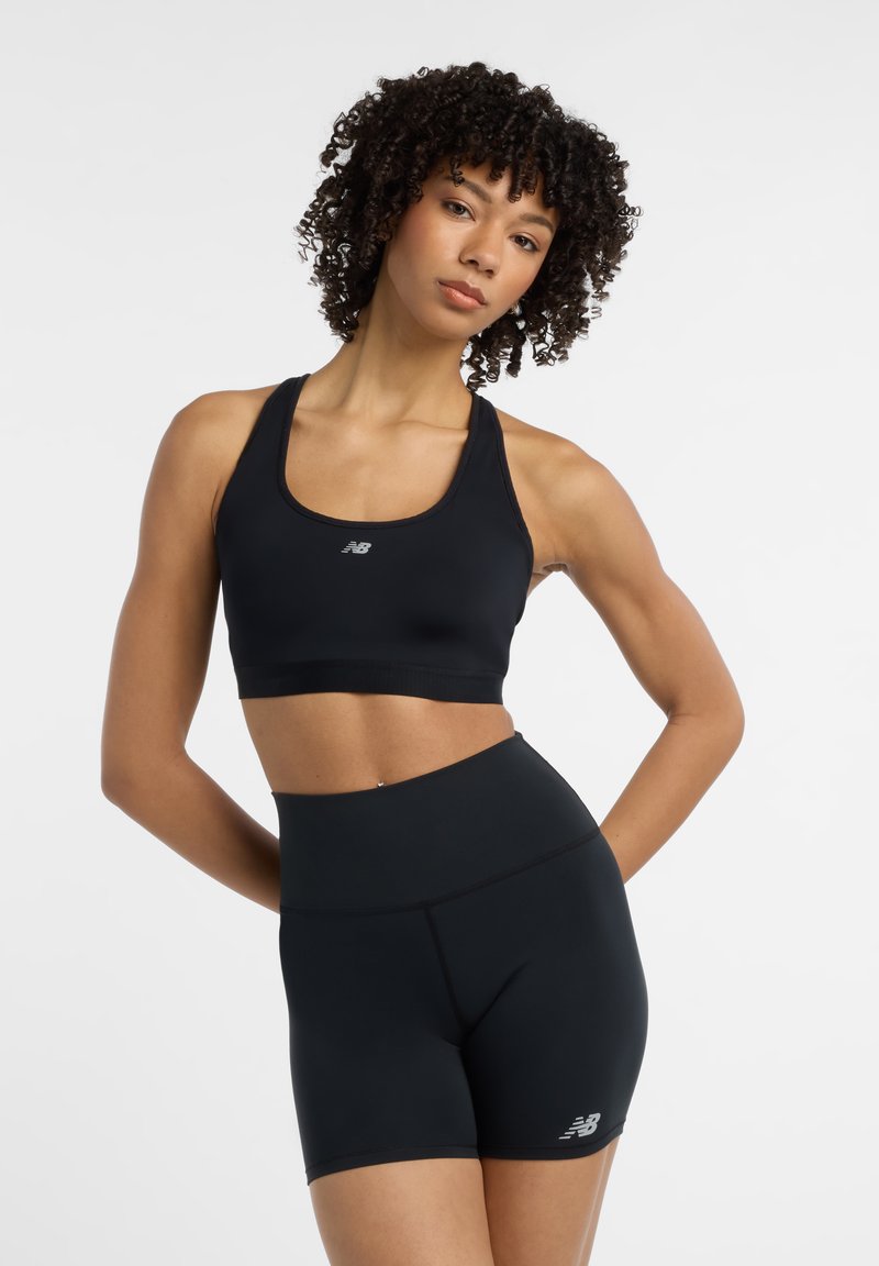 Soutien-gorge de sport noir et shorts taille haute en matériau extensible. Présente un logo sur la poitrine et la jambe. Texture lisse et design ajusté.